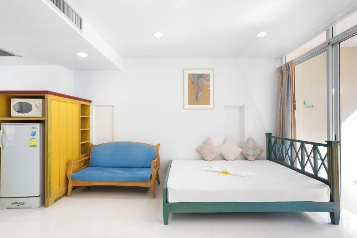 Un dormitorio con cama, una silla, un escritorio con computadora y una ventana.