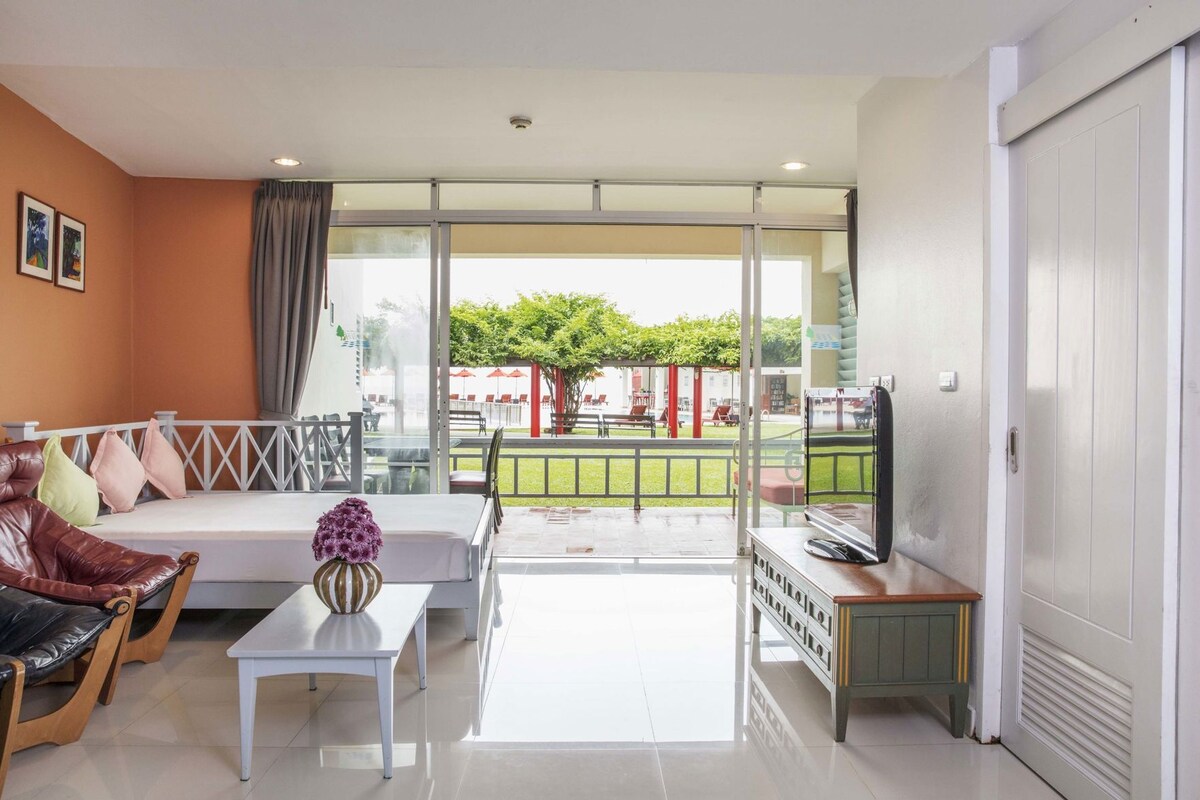 A modern living room with a sofa, a coffee table, and a TV. There is a balcony with a view of the outside.