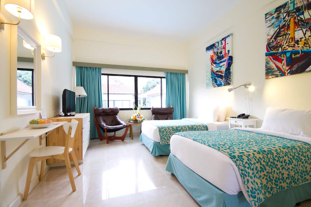 A hotel room with two beds, a desk, a chair, a TV, and a window with curtains.