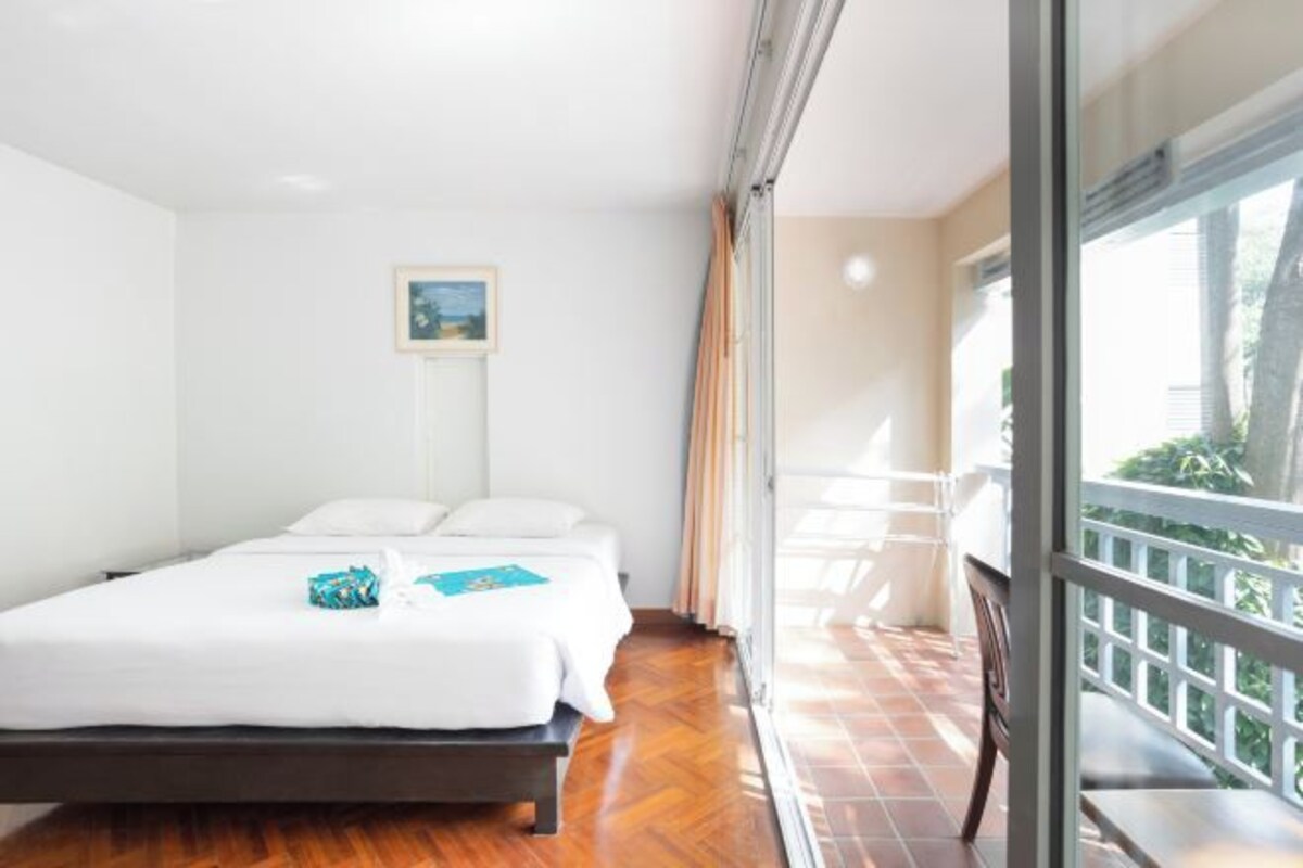 A hotel room with a bed, a small table, and a balcony with a view.