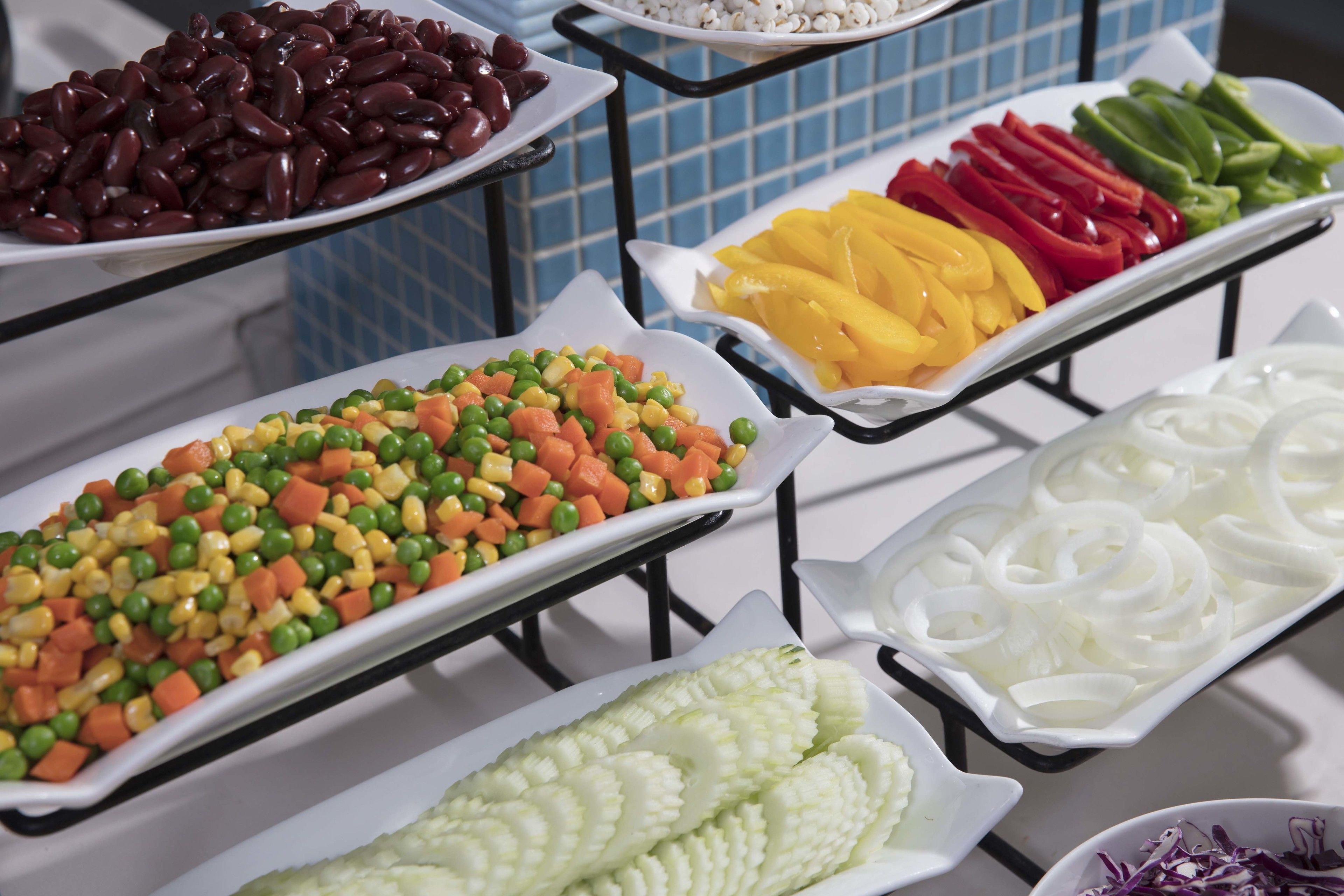 Ein Buffet mit verschiedenen Gerichten, darunter Bohnen, gemischtem Gemüse, Paprika und Zwiebeln.