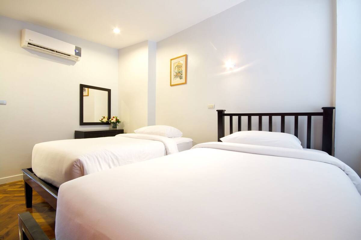 A hotel room with two beds, a mirror, an air conditioner, and a framed picture on the wall.