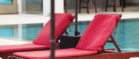 A poolside area with red lounge chairs and a table.