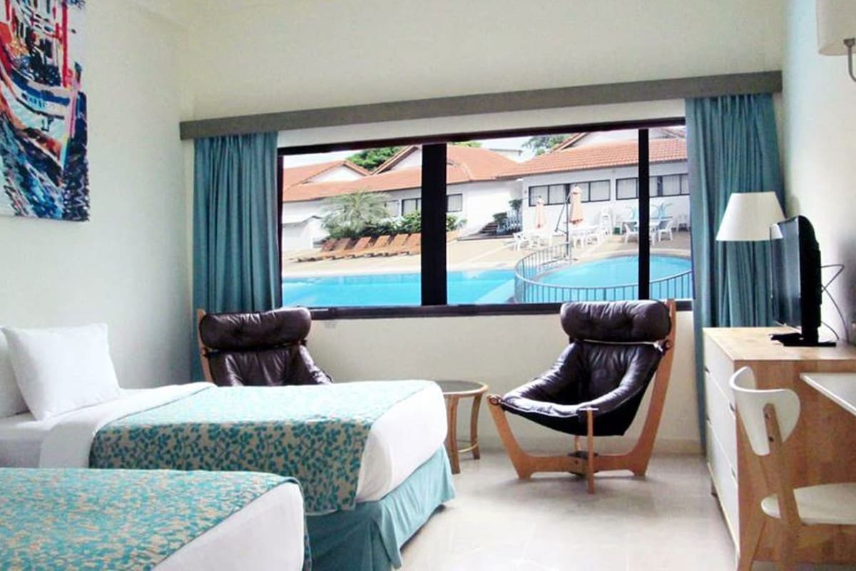 A hotel room with a bed, two chairs, a desk, a lamp, and a view of a swimming pool.