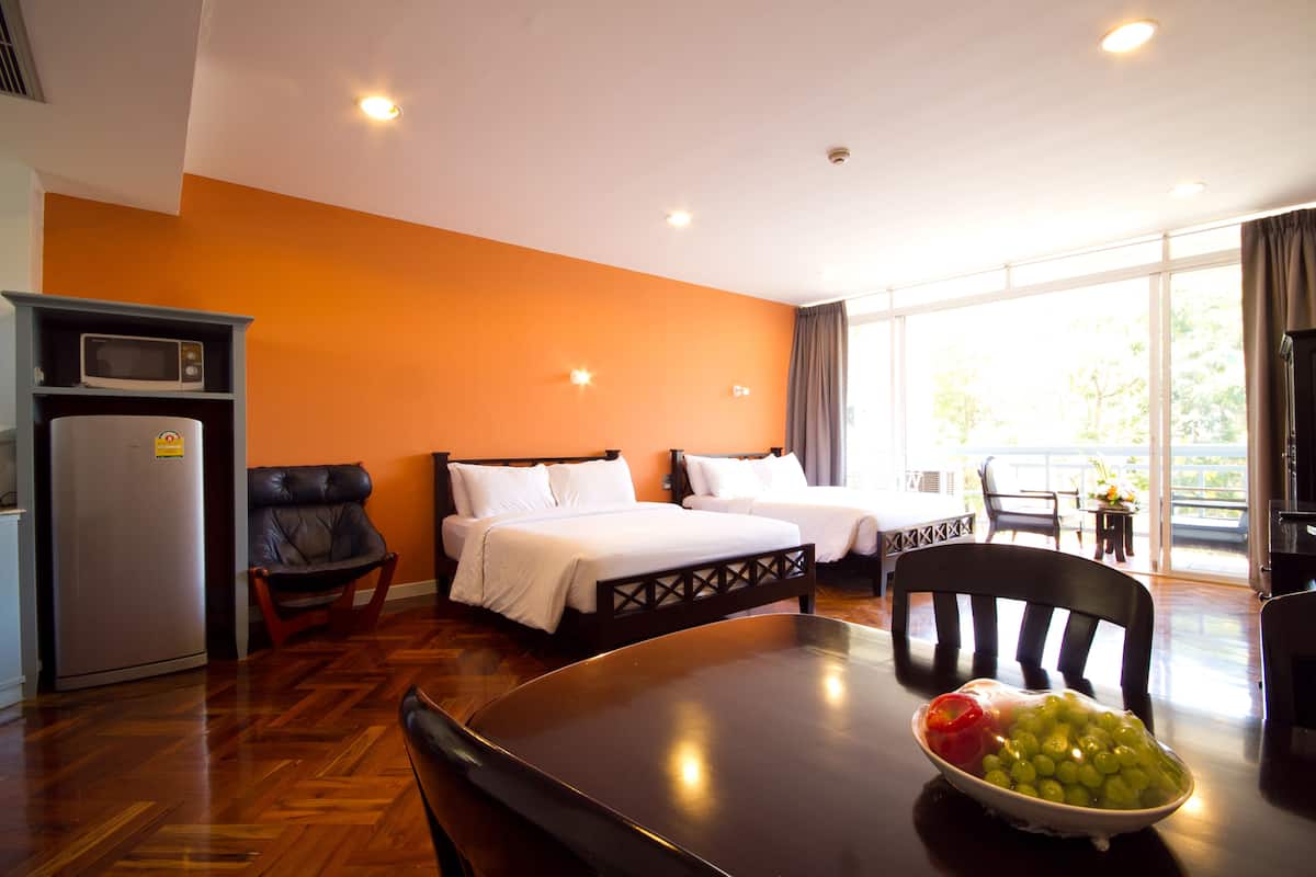 A hotel room with two beds, a dining table with a bowl of fruit, a microwave, and a view of the outdoors.