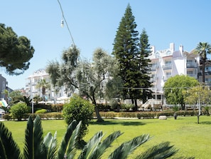 A park with grass, trees, and a building with balconies in the background. - Halıcı Hotel (Marmaris)