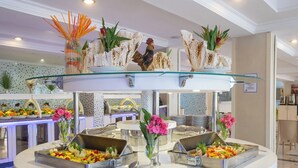 Disposição de buffet com várias estações de serviço, prateleira de vidro e elementos decorativos como flores e plantas.