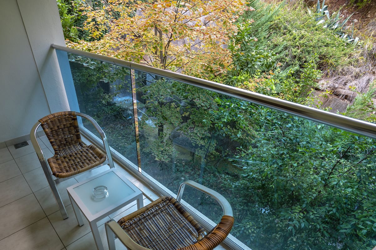 A balcony with two wicker chairs and a small table, overlooking a lush garden.