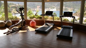 A gym with treadmills, an elliptical, and exercise balls, overlooking a scenic coastal area. - Turunc Resort (Marmaris)