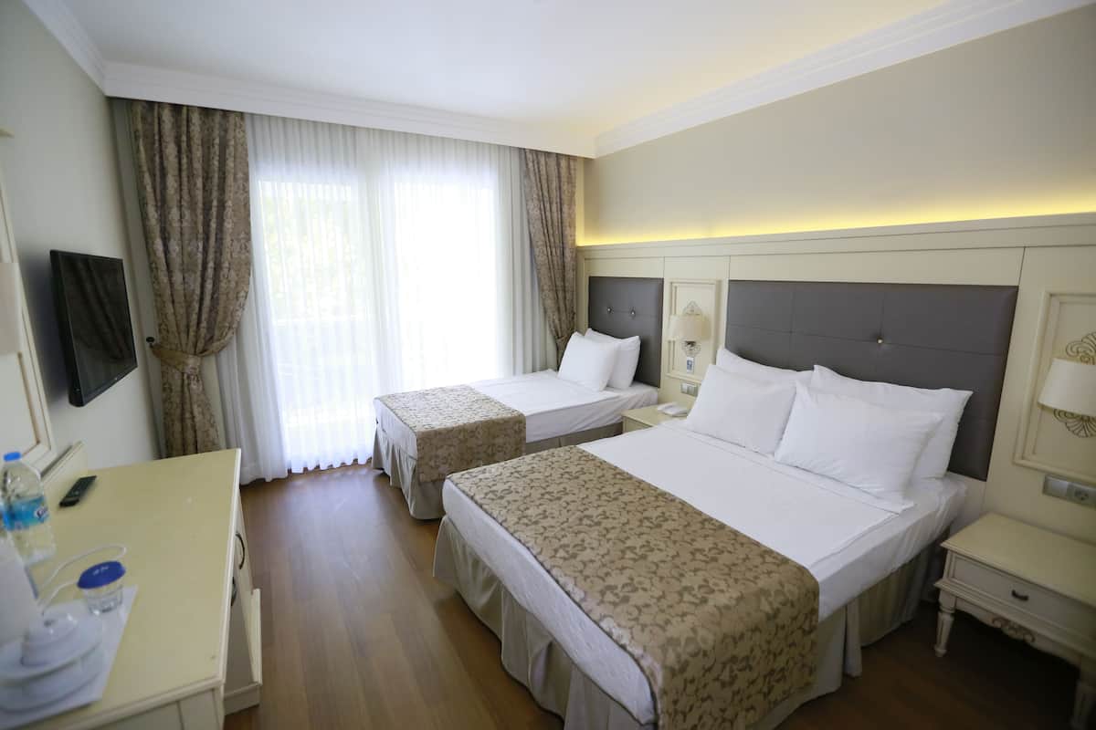 A hotel room with two beds, a desk, a chair, a TV, and a window with curtains.