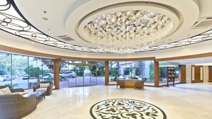 A spacious lobby with a large chandelier, comfortable seating, and large windows offering a view of the parking area. - Turunc Resort (Marmaris)