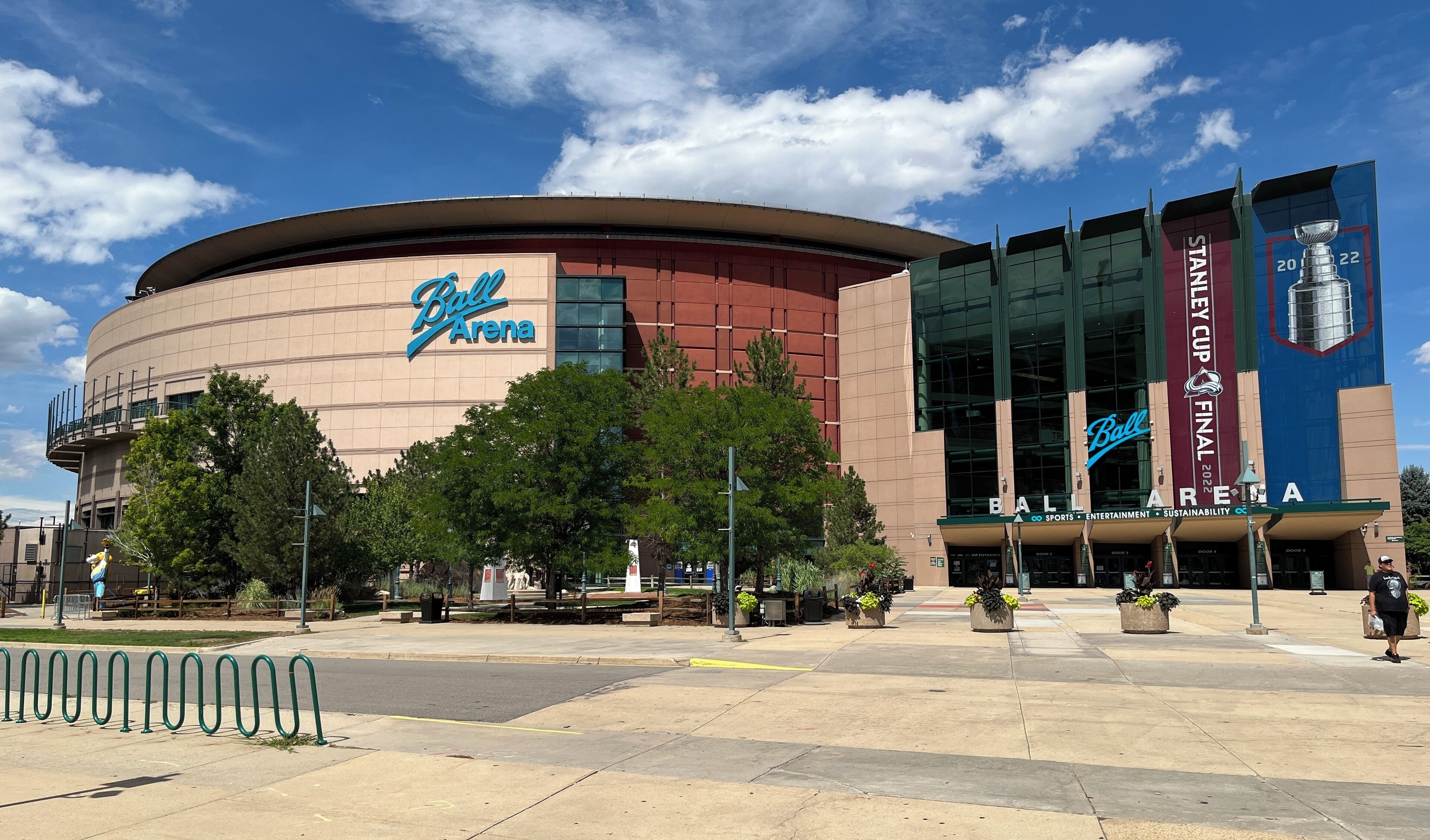 A large stadium with a prominent 'Ball Arena' sign, multiple doors, and a large blue banner advertising the Stanley Cup Final 2022.