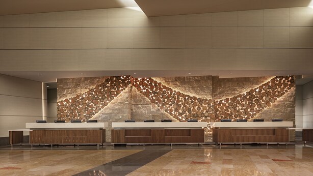 A modern reception area with a long counter, a stone wall with circular patterns, and a polished floor. - Hyatt Regency Denver at Colorado Convention Center (Denver)