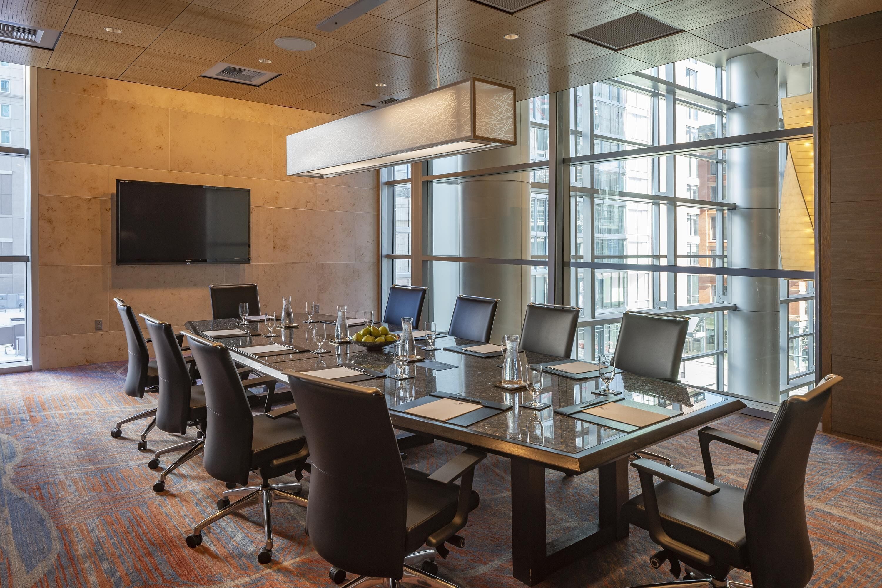 A conference room with a long table, chairs, a flat-screen TV, and large windows.