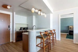 A modern kitchen with a central island, bar stools, a microwave, and a sink.