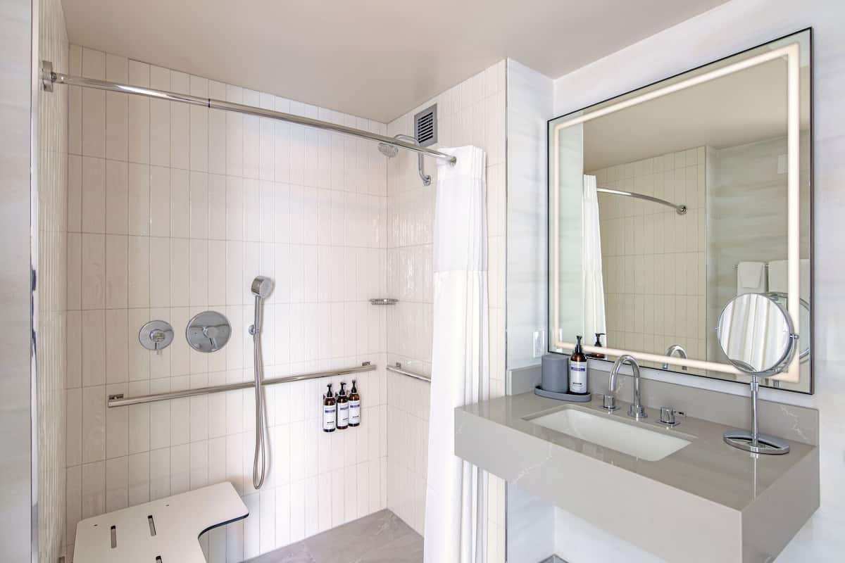 Un baño moderno con cabina de ducha, un espejo grande y un tocador con lavabo y artículos de aseo.