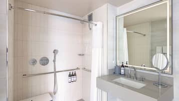 Un baño moderno con cabina de ducha, un espejo grande y un tocador con lavabo y artículos de aseo.