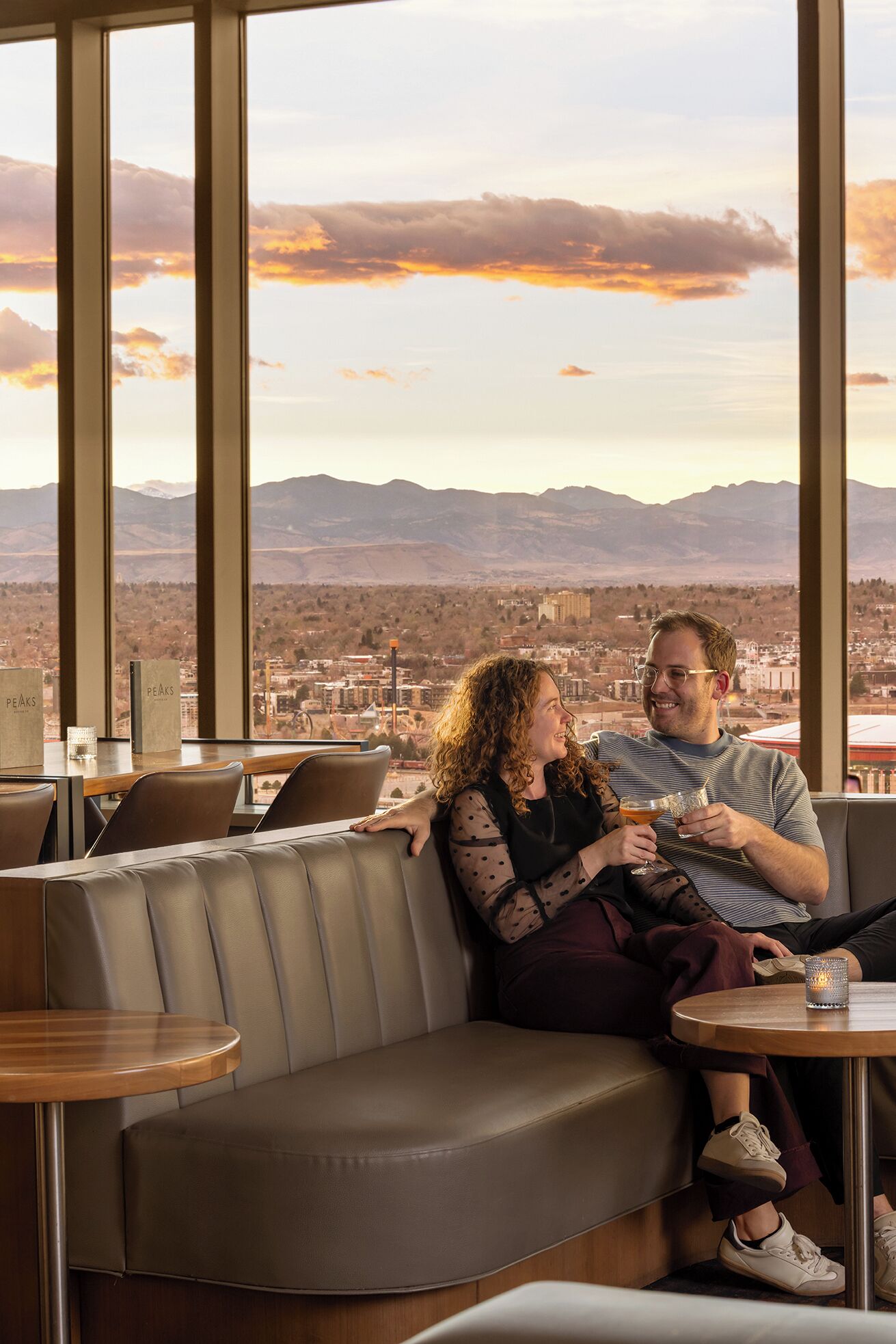 A couple seated on a leather couch with a cityscape view through large windows.