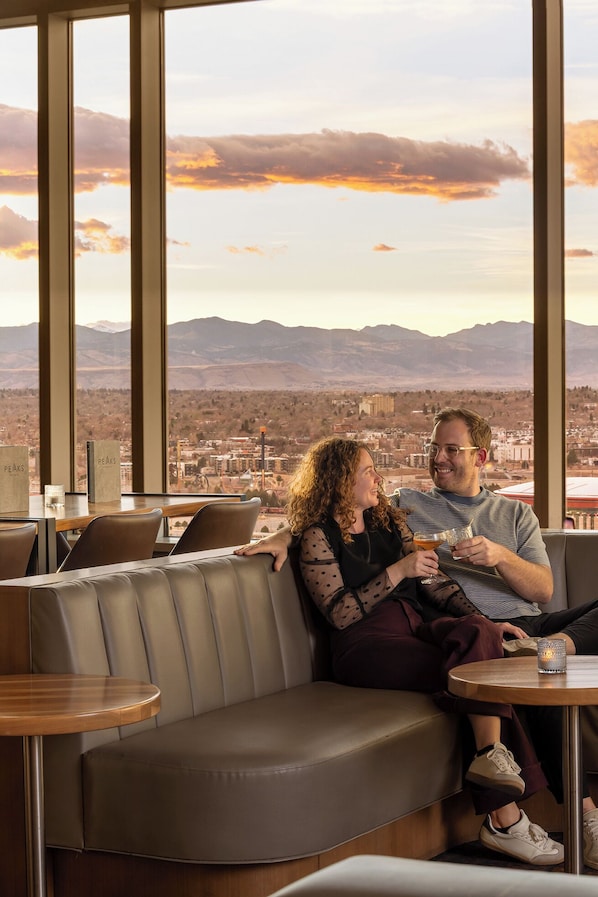 A couple seated on a leather couch with a cityscape view through large windows.