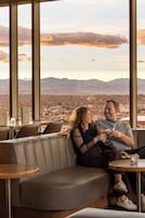 A couple seated on a leather couch with a cityscape view through large windows.