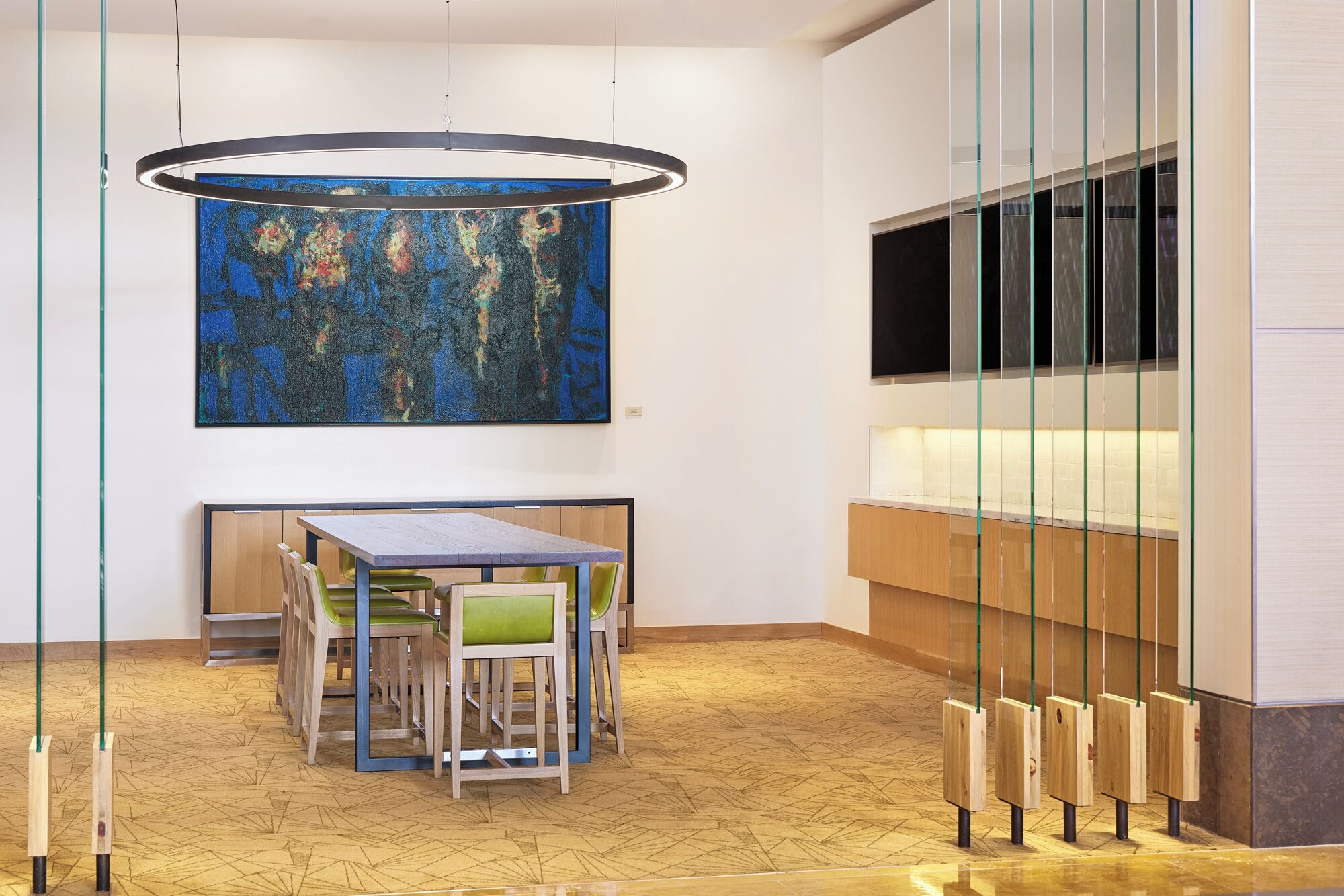 A modern interior with a wooden floor, a table with chairs, a large abstract painting, and a TV mounted on a glass partition.