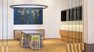 A modern interior with a wooden floor, a table with chairs, a large abstract painting, and a TV mounted on a glass partition.
