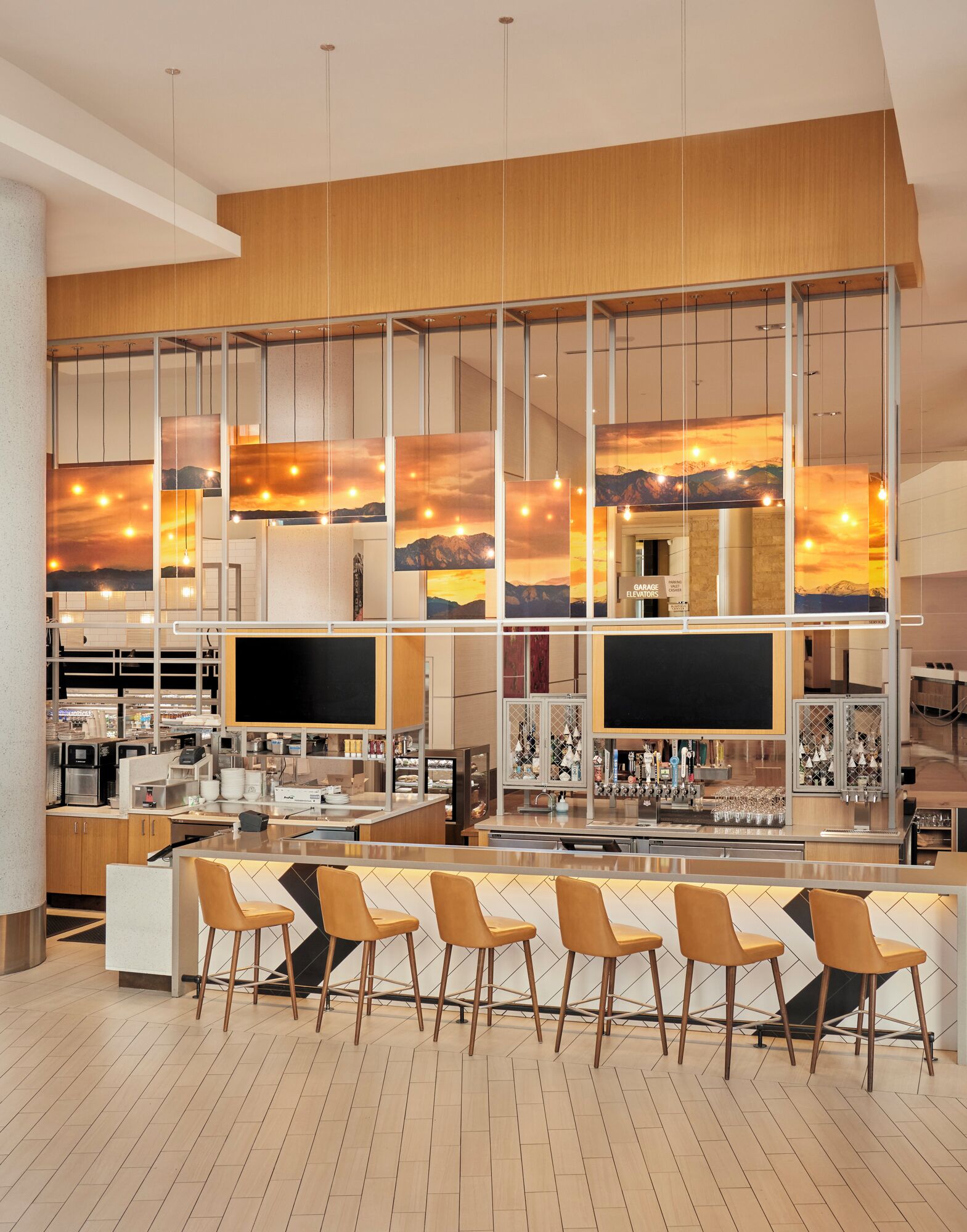 A modern bar area with a bar counter, multiple seating options, and a large window displaying a sunset view.