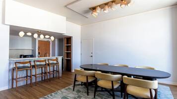 A dining area with a long table and six chairs, a bar area with stools, and a kitchen visible through an open door.