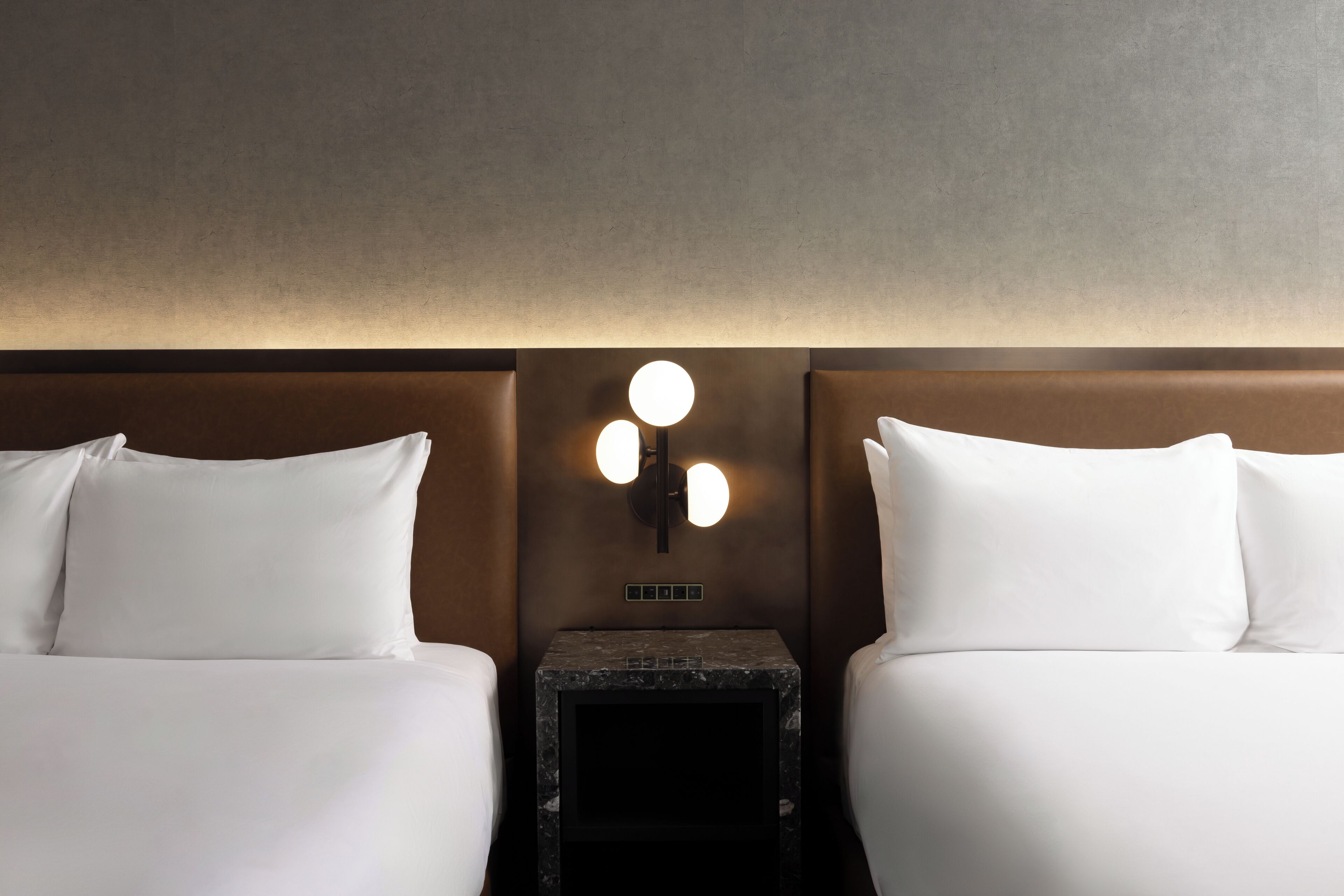 A hotel room with two beds, a nightstand, and a wall-mounted light fixture.