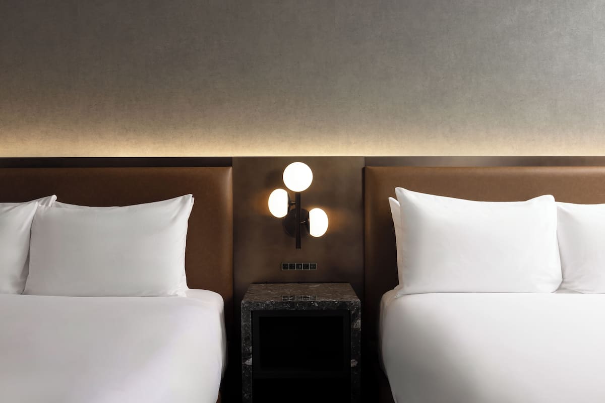 A hotel room with two beds, a nightstand, and a wall-mounted light fixture.
