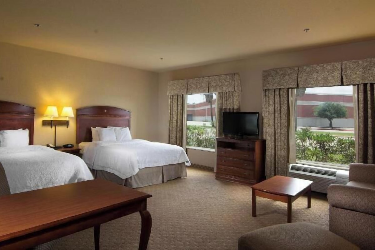 A hotel room with two beds, a TV, a desk, and a chair.