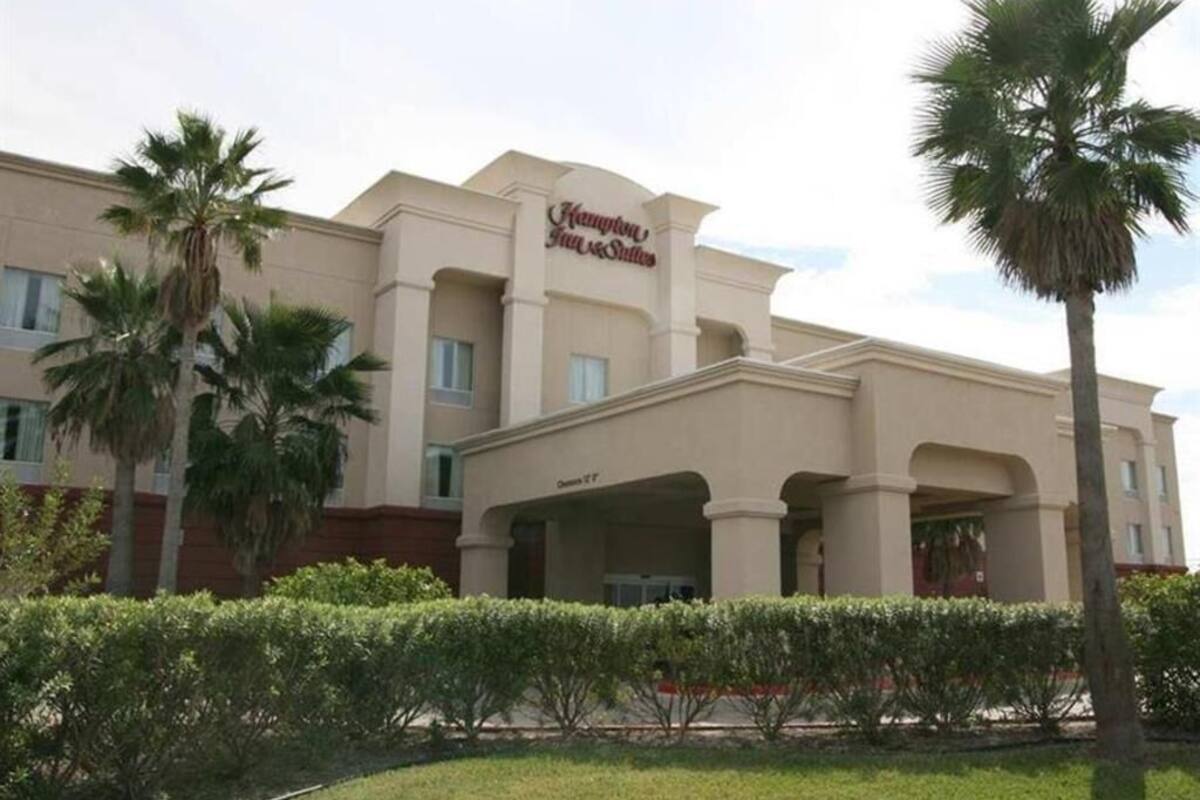 A hotel with a large entrance, palm trees, and a clear sky.