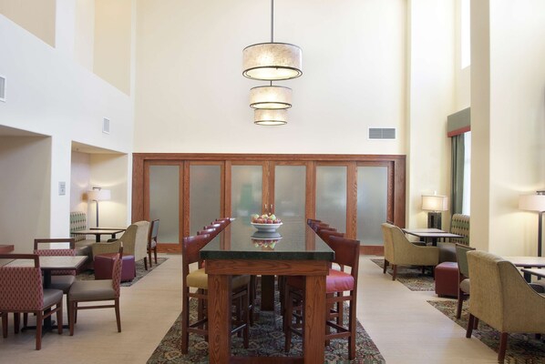 Un vestíbulo amplio con una mesa de comedor central rodeada de sillas, una lámpara colgante y un cuenco decorativo con fruta.