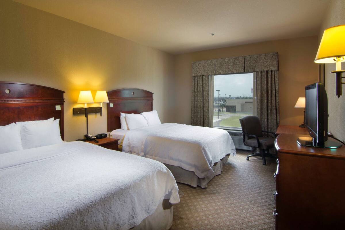 A hotel room with two beds, a desk, a chair, a television, and a window with curtains.