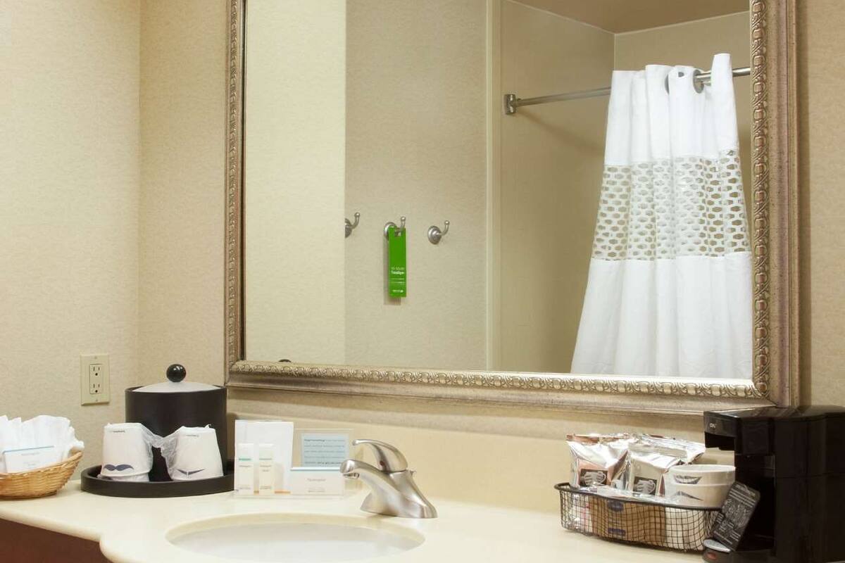 A hotel bathroom with a large mirror, a sink, toiletries, and a shower curtain.
