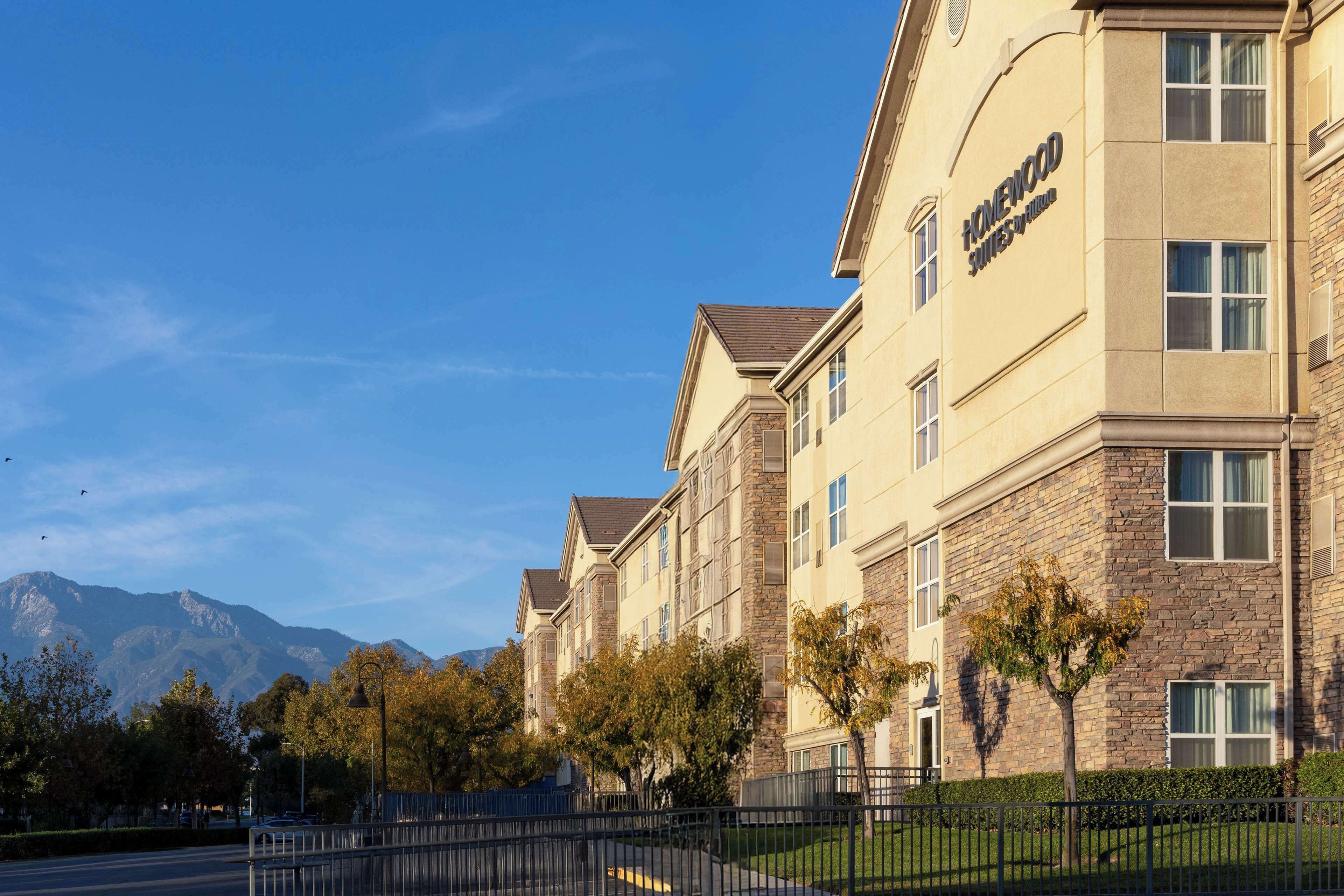 A multi-story hotel with a stone facade, large windows, and a clear view of mountains in the background.