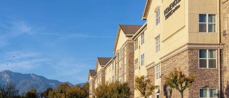 A multi-story hotel with a stone facade, large windows, and a clear view of mountains in the background.