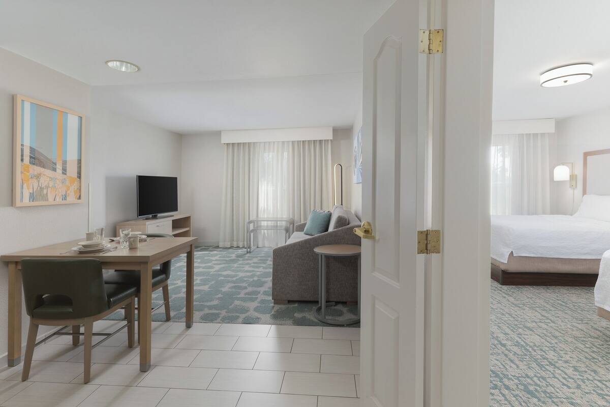 A hotel room with a bed, a desk with a chair, a sofa, a TV, and a small table.