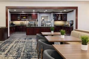 Une cuisine moderne avec des meubles de couleur bois foncé, un îlot central doté d’un évier et un coin salon agrémenté d’un tapis et de chaises.