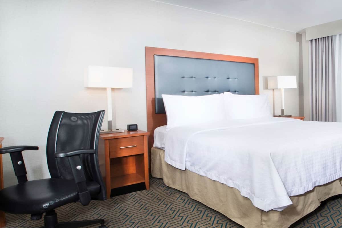 Een hotelkamer met een bed, een bureau, een stoel, een televisie en een raam met gordijnen.