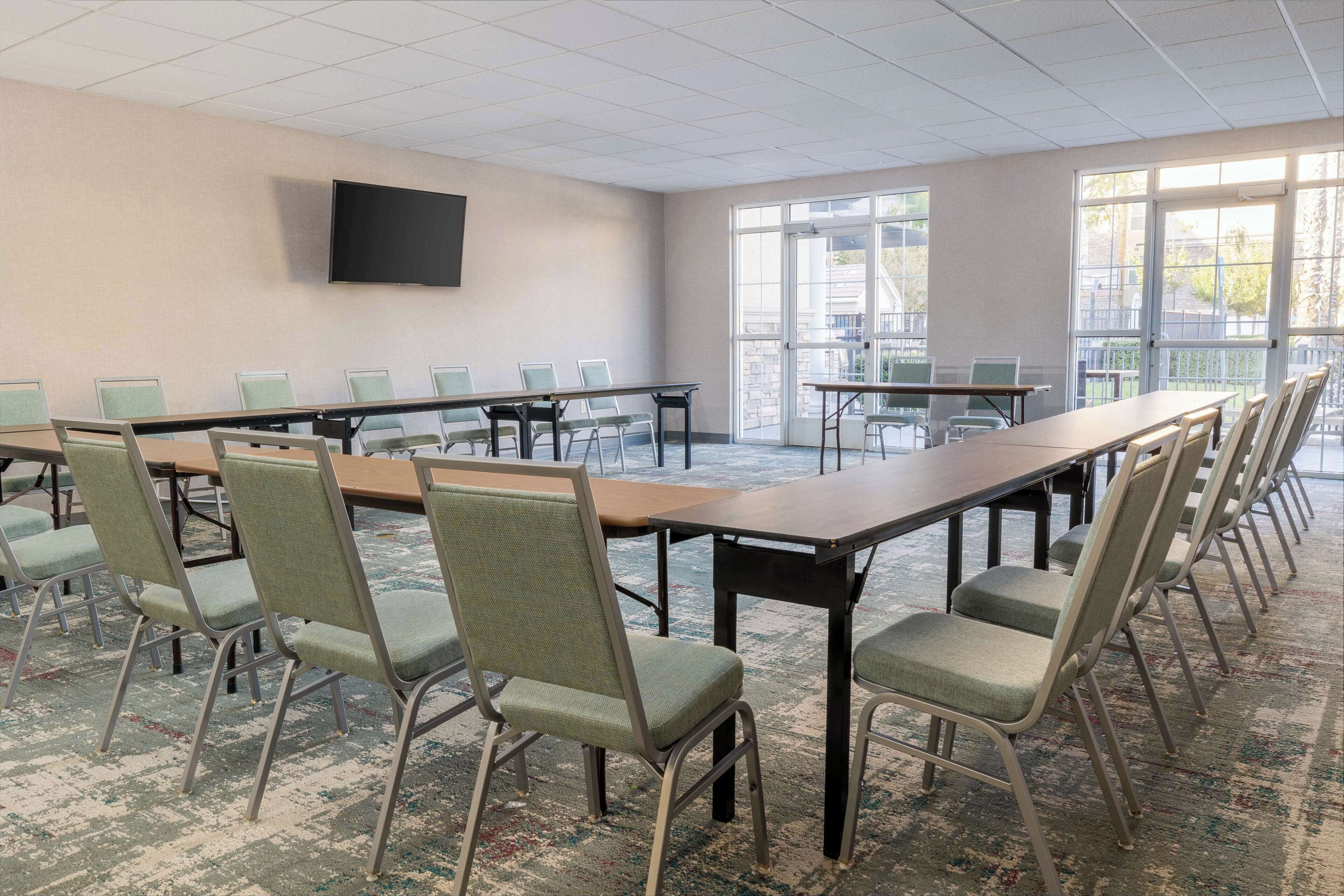 A conference room with a long table, multiple chairs, a flat-screen TV, and large windows.