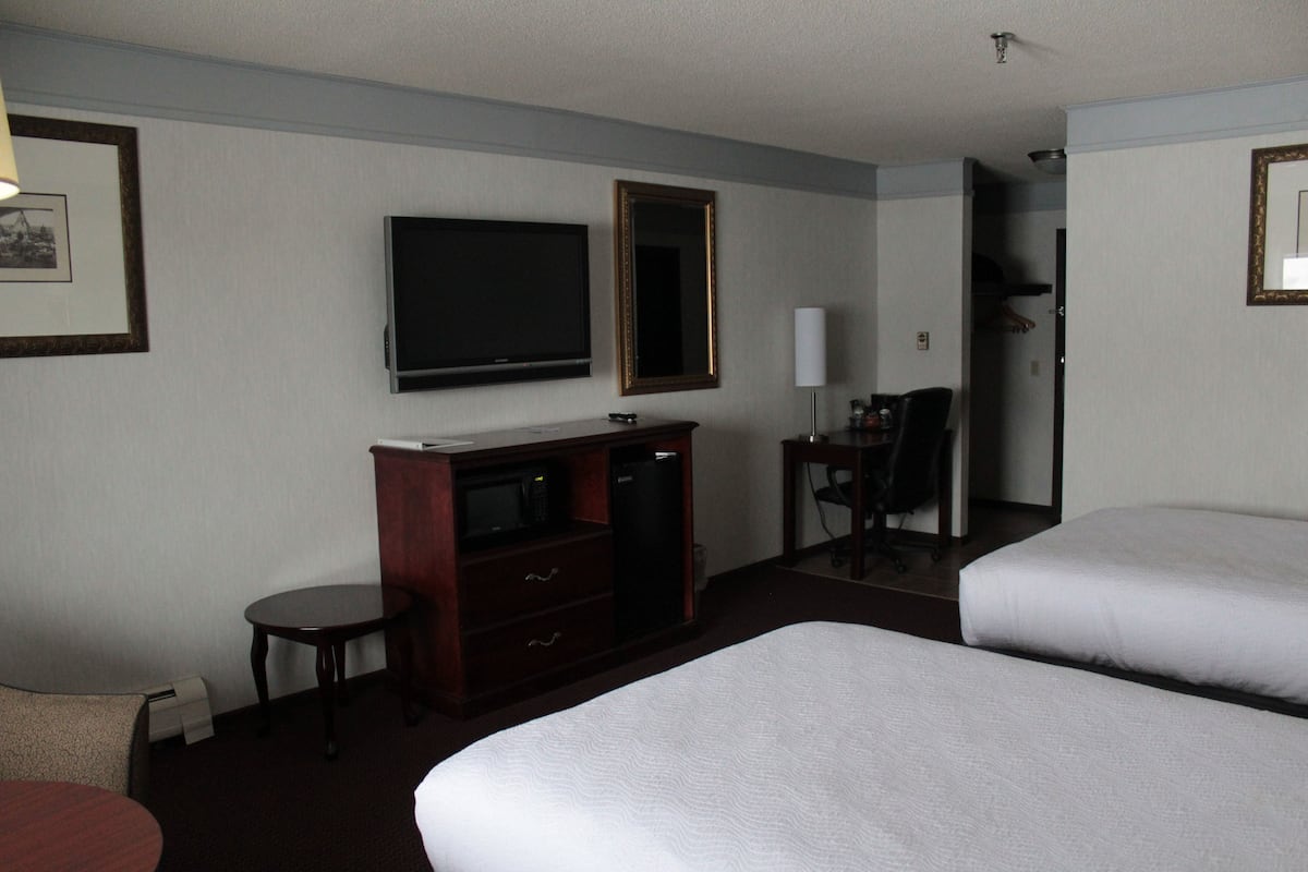 Habitación de hotel con dos camas, un escritorio, una silla, un televisor y un espejo.