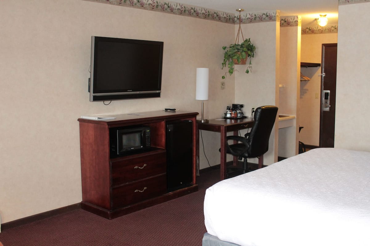 Una habitación de hotel con cama, escritorio, computadora, televisión, microondas y cafetera.