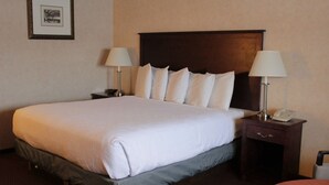 A neatly made bed with white linens, a wooden headboard, two bedside tables with lamps, and a framed picture on the wall.