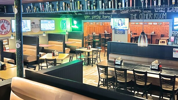 A restaurant with booths and tables, a bar area with various beer taps, and a chalkboard menu.