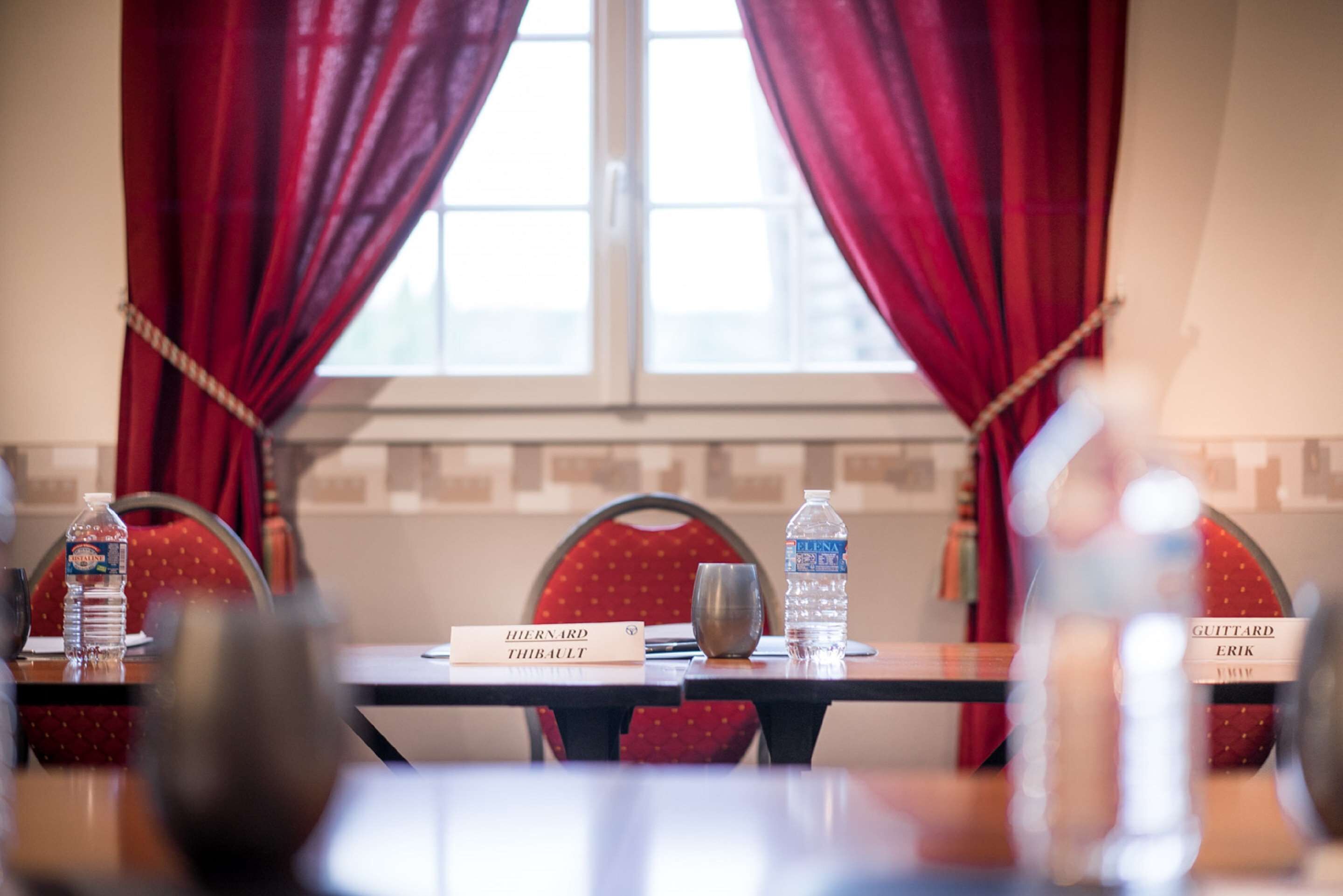 A conference room with nameplates, water bottles, and a window with red curtains.