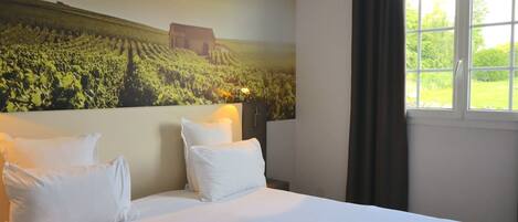 Habitación de hotel con una cama grande, dos almohadas, una mesita de noche y un mural en la pared de un viñedo.