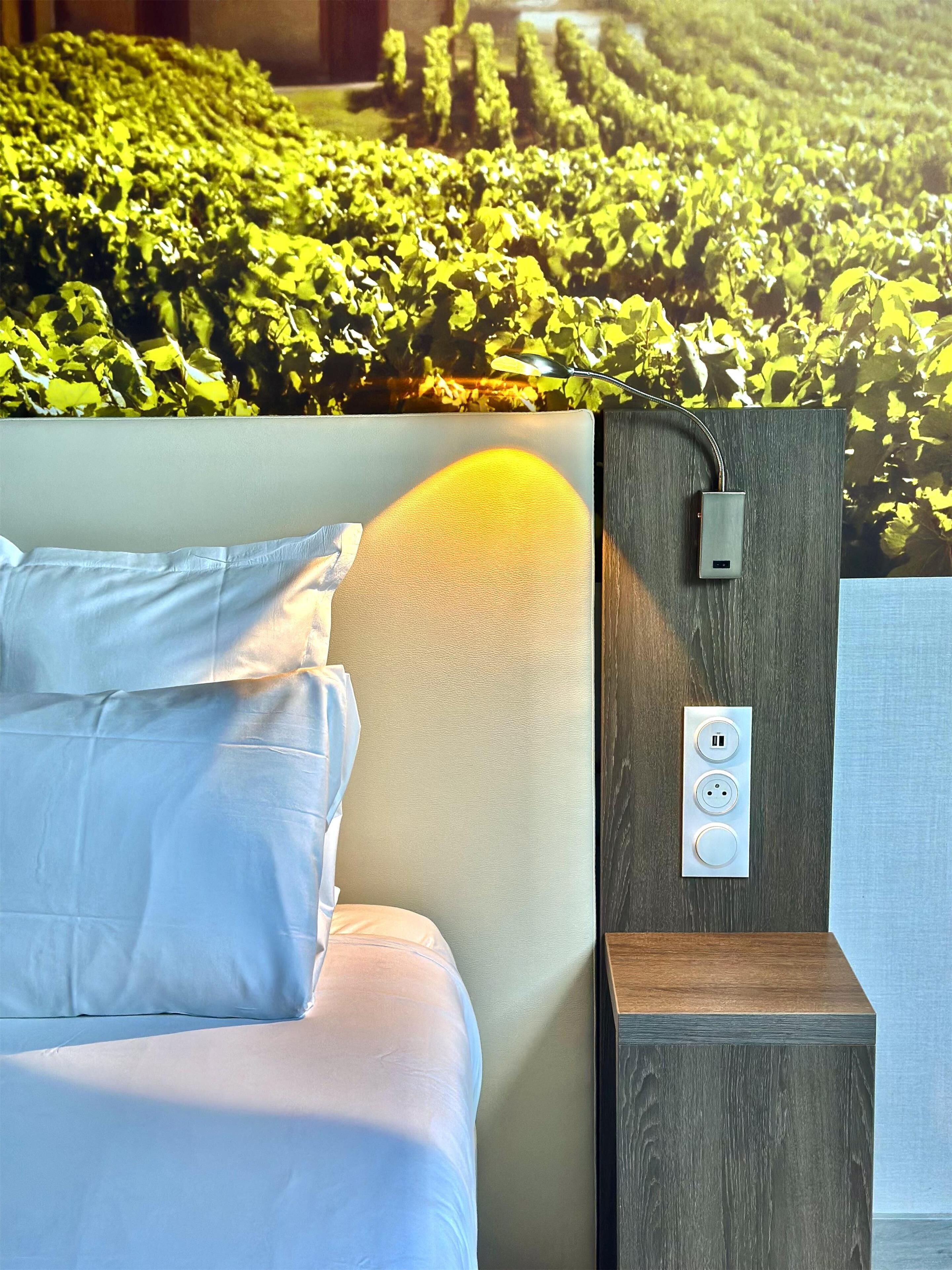 Un dormitorio con cama, un enchufe en la pared y un ventanal con vistas a un viñedo.