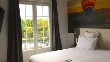 A hotel room with a large bed, a window with curtains, and a painting of a hot air balloon.