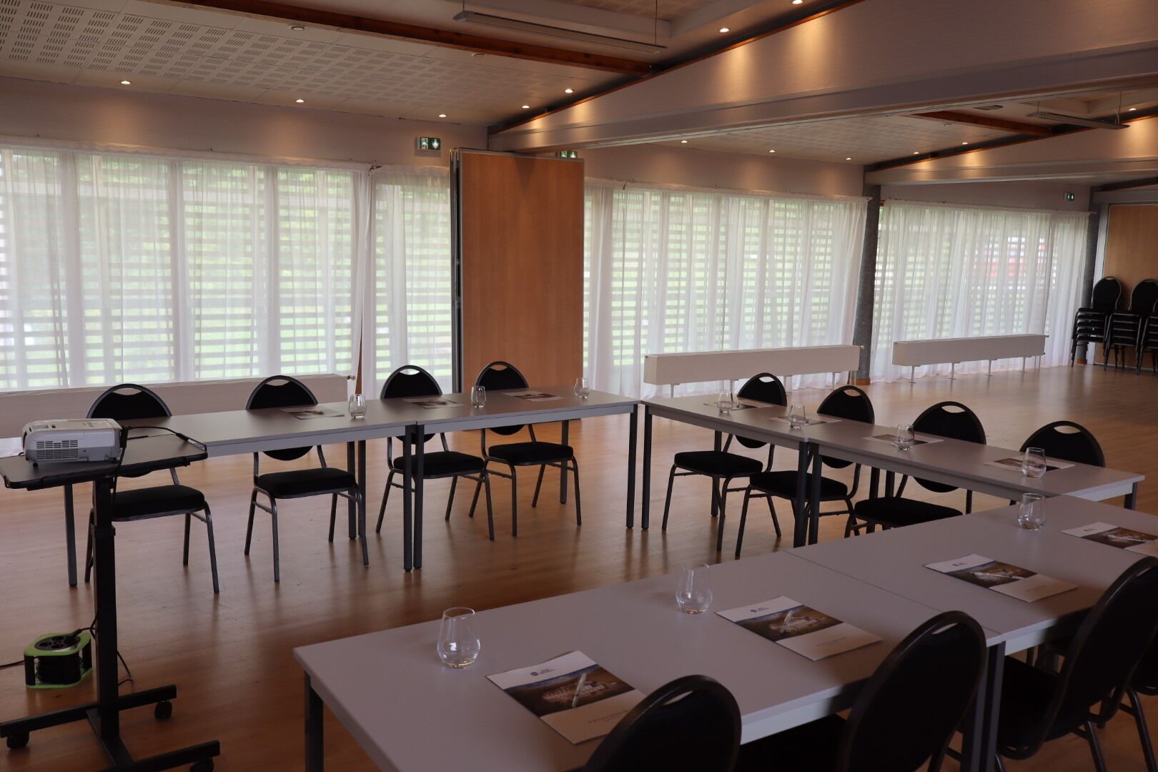 Une salle de conférence avec de longues tables, des chaises noires et un projecteur.